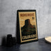 A metal sign with a mountain landscape and the text "MONUMENT COLORADO" printed on it, placed on a countertop next to some black camera lenses.