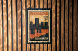 A vintage postage stamp from Virginia, featuring a cityscape and a bridge, is displayed on a wooden wall.