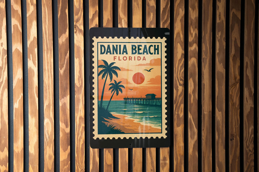 A vintage-style poster of Dania Beach, Florida, featuring palm trees, a sunset, and a pier, is displayed on a wooden wall.