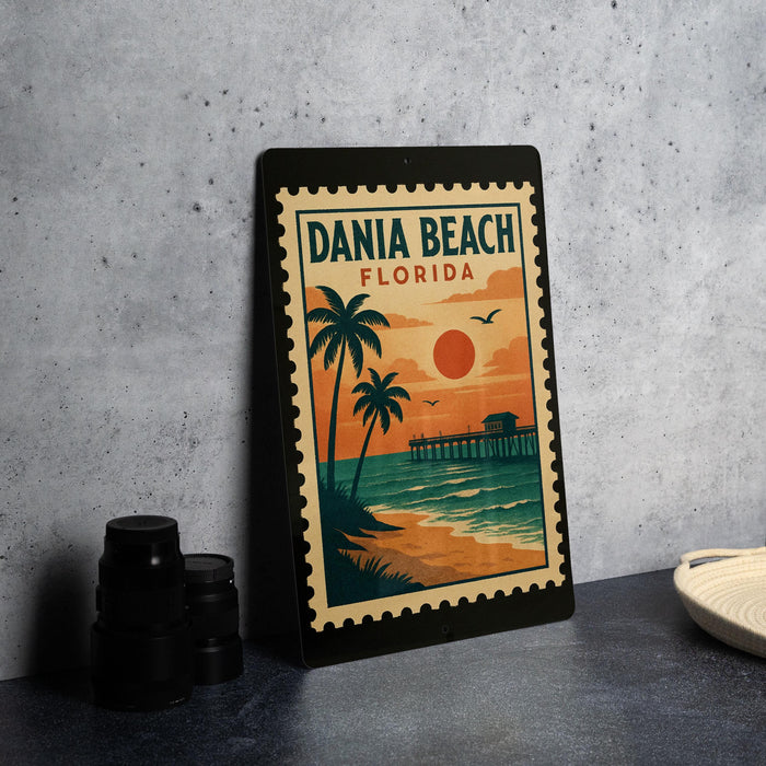 A framed poster of a tropical beach scene with palm trees, a pier, and a sunset is displayed on a table.