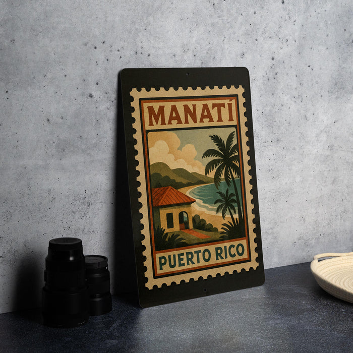 A vintage-style poster of Manati, Puerto Rico, featuring a tropical landscape with palm trees and a house, is displayed on a wall.