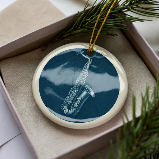 A ceramic ornament in a white box, featuring a saxophone design on a blue background.