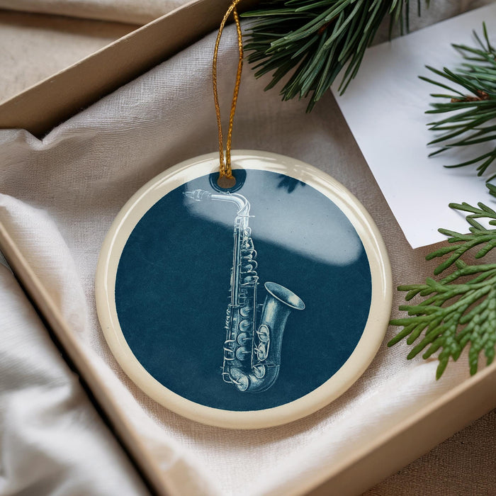 A blue ornament with a white saxophone design is displayed in a box, surrounded by pine branches.
