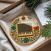 A decorative ornament featuring a musical keyboard and flowers is displayed in a box, surrounded by pine branches.