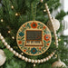 A round ornament with a musical keyboard design is hanging on a Christmas tree, surrounded by ornaments and lights.