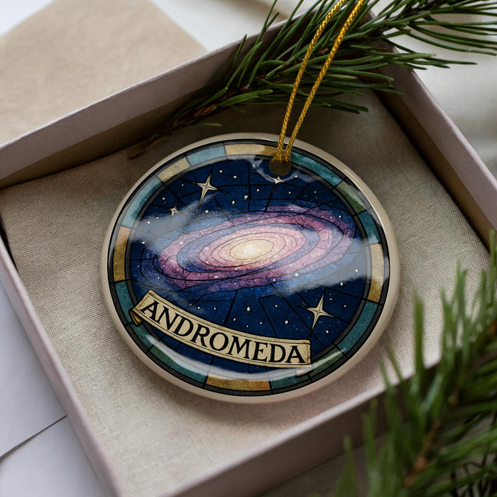 A decorative ornament in a box, featuring a colorful depiction of a galaxy and the word "ANDROMEDA" written on it.