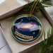 A decorative ornament in a box, featuring a colorful depiction of a galaxy and the word "ANDROMEDA" written on it.