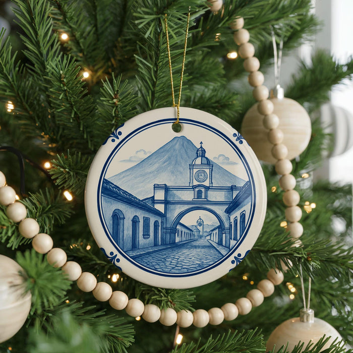A Christmas tree decorated with ornaments, including a ceramic ornament featuring a blue and white illustration of a building with a clock tower.