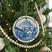 A Christmas tree decorated with ornaments, including a ceramic ornament featuring a blue and white illustration of a building with a clock tower.