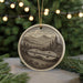 A round ornament featuring a black and white illustration of a lute or banjo, set against a mountainous landscape with trees and a river.