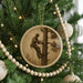 A round ornament on a Christmas tree featuring a man in a hard hat and safety harness, climbing a tree.