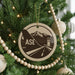 A Christmas tree decorated with ornaments, including a circular ornament with a graphic of a plane and a mountain range.