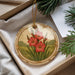 A decorative ornament with a floral design, featuring red flowers and green foliage, is displayed in a box with pine branches.