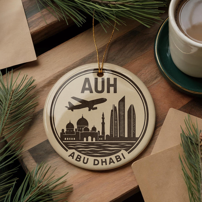 A circular ornament with a graphic of Abu Dhabi skyline and an airplane, placed on a wooden surface next to a cup of coffee and some pine branches.