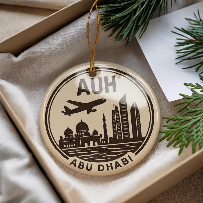 A circular ornament with a graphic of the Abu Dhabi skyline and an airplane, placed on a beige surface next to some pine branches.