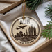 A circular ornament with a graphic of the Abu Dhabi skyline and an airplane, placed on a beige surface next to some pine branches.
