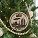 A Christmas tree decorated with ornaments, including a circular ornament with a graphic of Abu Dhabi skyline and the text "AUH" and "ABU DHABI".