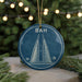 A blue circular ornament with a white illustration of a tall building and palm trees, hanging from a string.