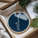 A blue ornament with a white saxophone design is displayed in a box, surrounded by pine branches.