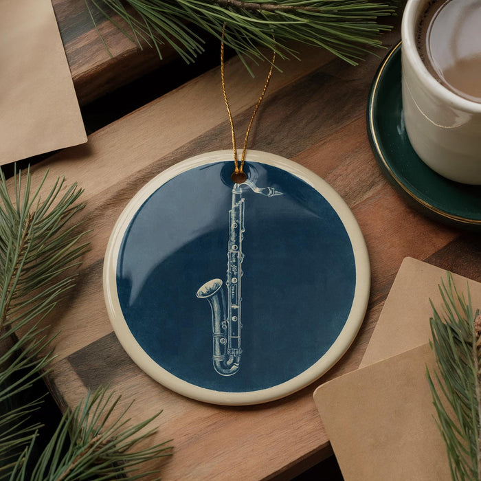 A blue ceramic ornament with a white saxophone design is displayed on a wooden surface, accompanied by a white mug and pine branches.