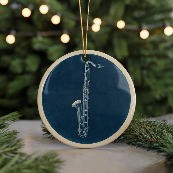 A blue ceramic ornament with a white saxophone design is displayed on a table, with a blurred background of a Christmas tree and twinkling lights.