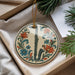 A decorative ornament in the shape of a flute, featuring a floral design, is displayed in a box alongside pine branches and a white card.