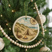 A Christmas tree decorated with a circular ornament featuring a camping scene with a tent, campfire, and compass.