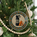 A Christmas tree ornament featuring a black spray bottle with a label that says "BEAR SPRAY" and an orange whistle, surrounded by a decorative border of beads.
