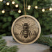 A round ornament featuring a detailed illustration of a bee on a beehive, surrounded by pine branches and twinkling lights in the background.