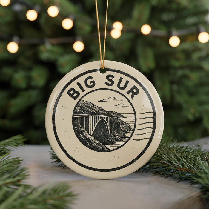 A ceramic ornament with the text "BIG SUR" and an illustration of a bridge, surrounded by greenery and twinkling lights.