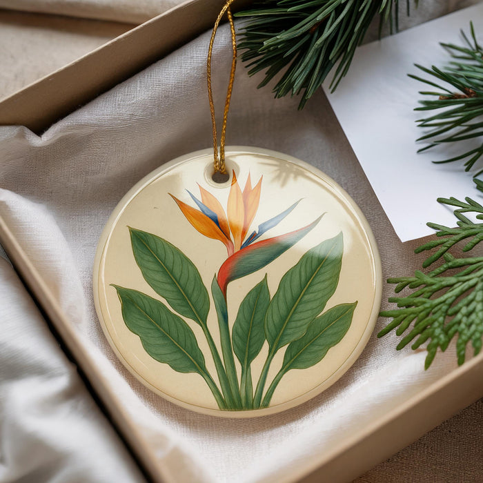 A decorative ornament with a floral design, featuring a large orange flower surrounded by green leaves, is displayed in a box with pine branches.