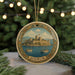 A decorative ornament featuring a castle on a body of water, surrounded by pine branches and holiday lights.