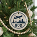 A Christmas tree decorated with ornaments, including a circular ornament with a silhouette of a city skyline and an airplane, and a beaded ornament.