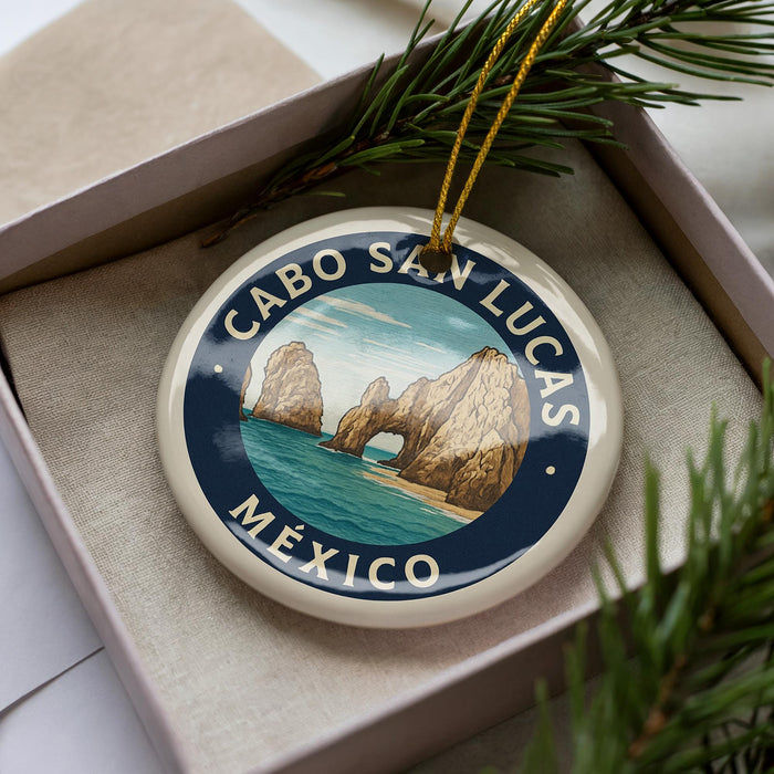 A decorative ornament with a circular design featuring a scenic image of Cabo San Lucas, Mexico, surrounded by pine branches.