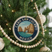 A Christmas tree decorated with ornaments, including a circular ornament with a scenic image of Cabo San Lucas, Mexico, surrounded by lights and greenery.