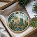 A decorative ornament featuring a cityscape of Calgary, Canada, with a bridge and trees, hanging from a string.