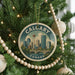 A circular ornament on a Christmas tree, featuring a cityscape of Calgary, Canada, with a bridge and trees in the background.