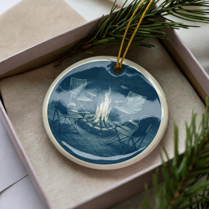 A ceramic ornament in a box, featuring a scene of two chairs around a campfire.