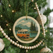 A Christmas tree decorated with ornaments, including a circular ornament featuring a van on a road surrounded by pine trees and mountains.
