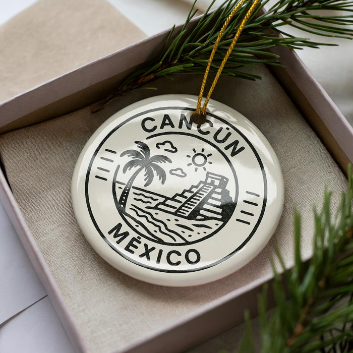 A ceramic ornament with the text "CANCUN MEXICO" printed on it, surrounded by a decorative border and a palm tree illustration.