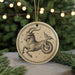 A decorative ornament featuring a stylized depiction of a goat or ram, with stars surrounding it, is displayed on a surface with pine branches in the background.