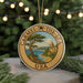 A round ornament with a painting of a coastal scene and a lighthouse, surrounded by greenery and a string of lights.