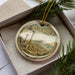 A decorative ornament in a box, featuring a landscape with a castle and a body of water.