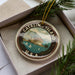 A circular ornament with a picture of Catalina Island, a U.S.A. landmark, surrounded by pine branches.
