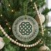 A Christmas tree decorated with ornaments, including a large circular ornament with a Celtic knot design, surrounded by green pine branches and white beads.