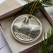 A decorative ornament featuring the Cologne Cathedral in Germany, displayed in a box with pine branches.