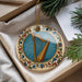 A decorative ornament featuring a harp is displayed in a box, surrounded by pine branches and a white card.