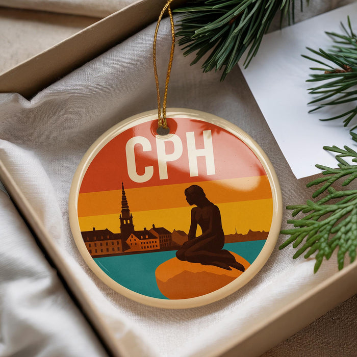 A round ornament with a silhouette of a person sitting on a rock, with a cityscape in the background, is displayed in a box.