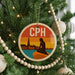 A Christmas tree decorated with ornaments, including a circular ornament with a silhouette of a person and a cityscape in the background.