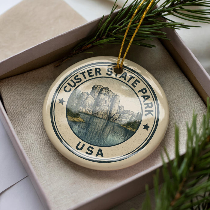 A decorative ornament in a box, featuring a circular design with a mountain landscape and water.